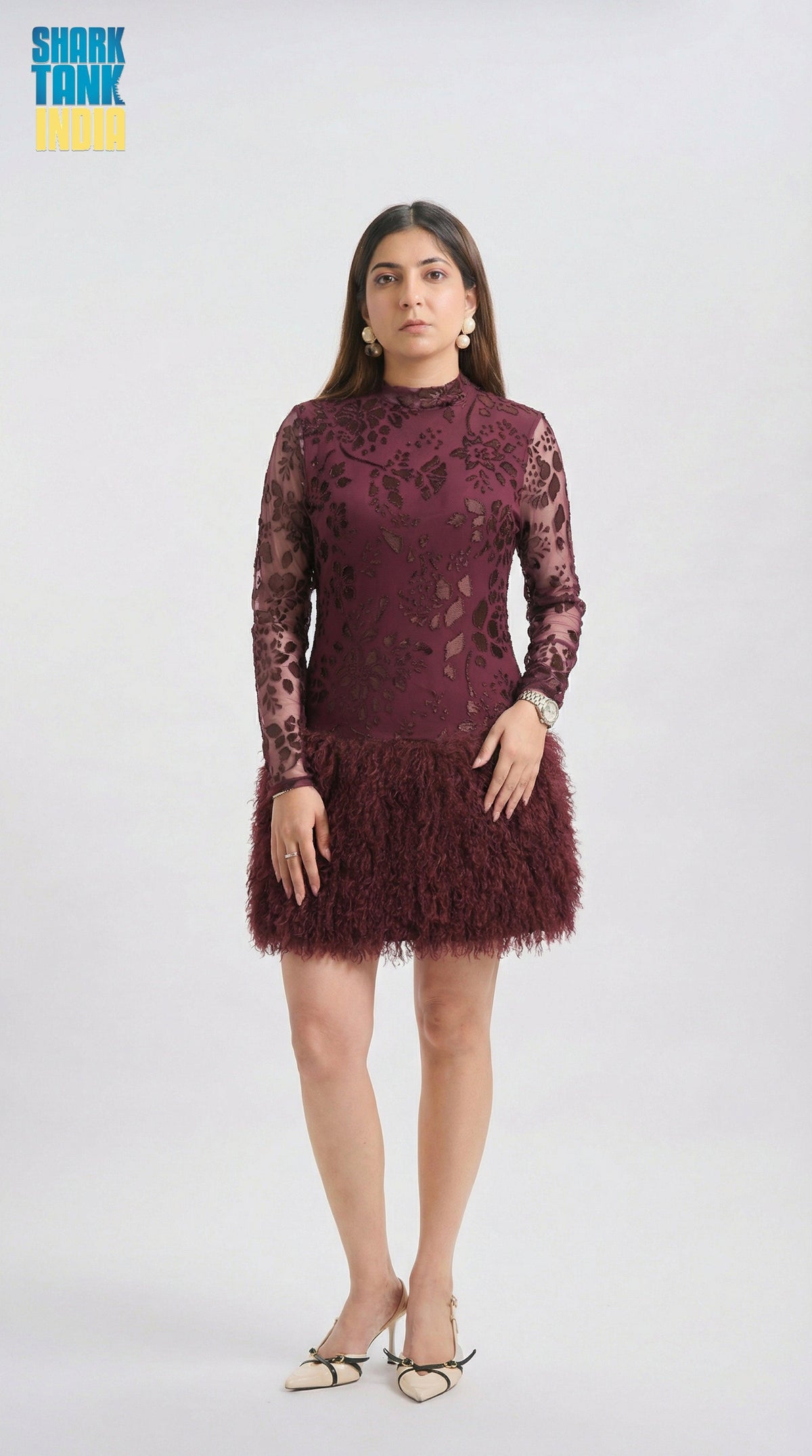 Woman wearing a burgundy lace dress with feathered skirt on a white background