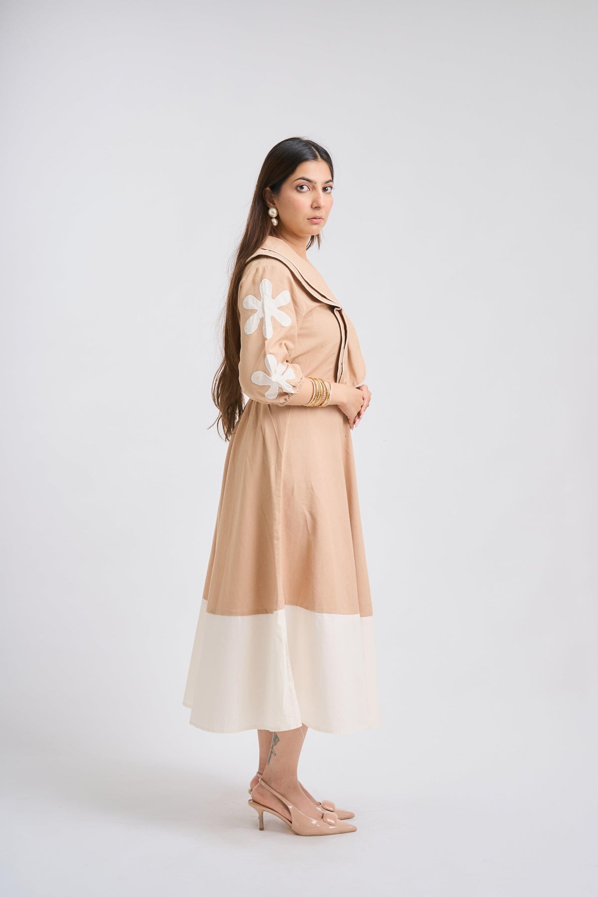 Woman wearing a beige dress with floral details on a white background