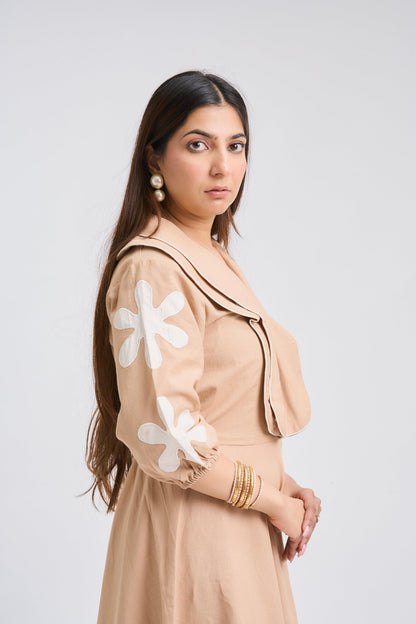 Woman wearing a beige dress with white floral patterns on a plain background