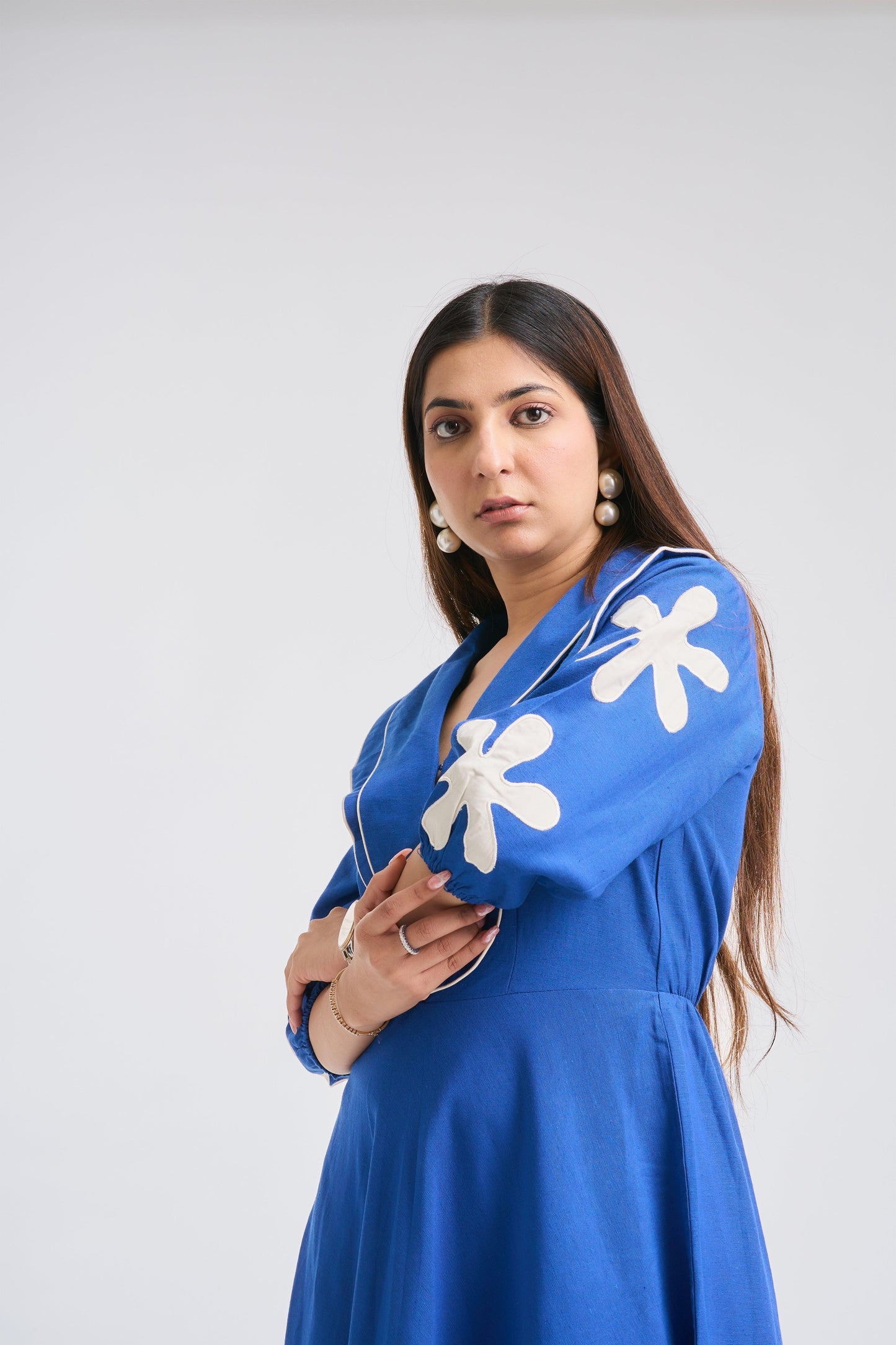 Woman wearing a blue dress with white floral patterns on a plain background