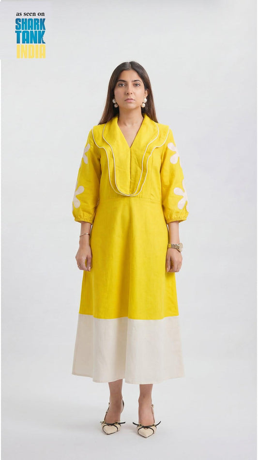 Woman wearing a yellow and white dress on a white background with 'Shark Tank India' branding.