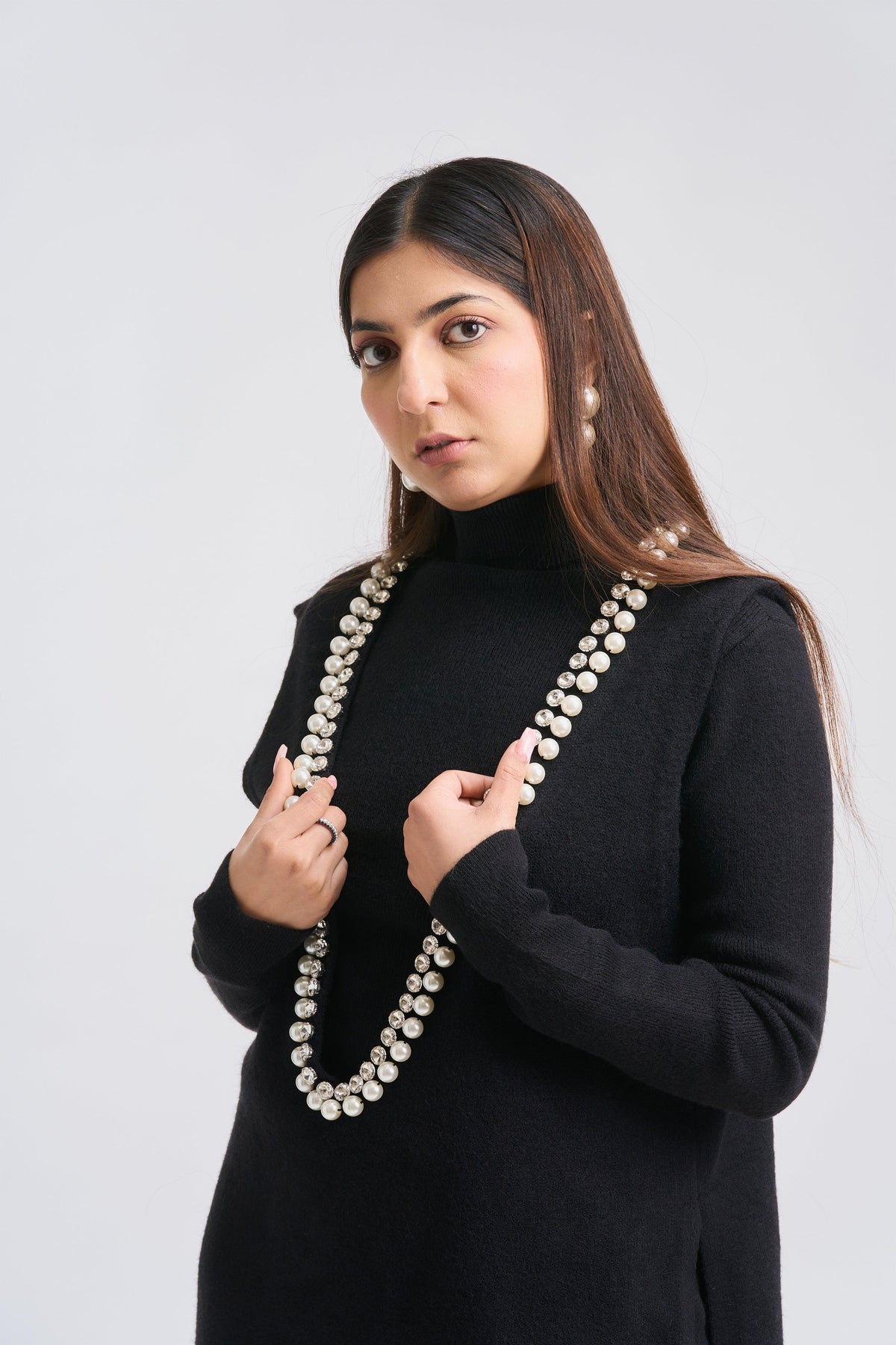 Woman wearing a long pearl necklace against a plain background