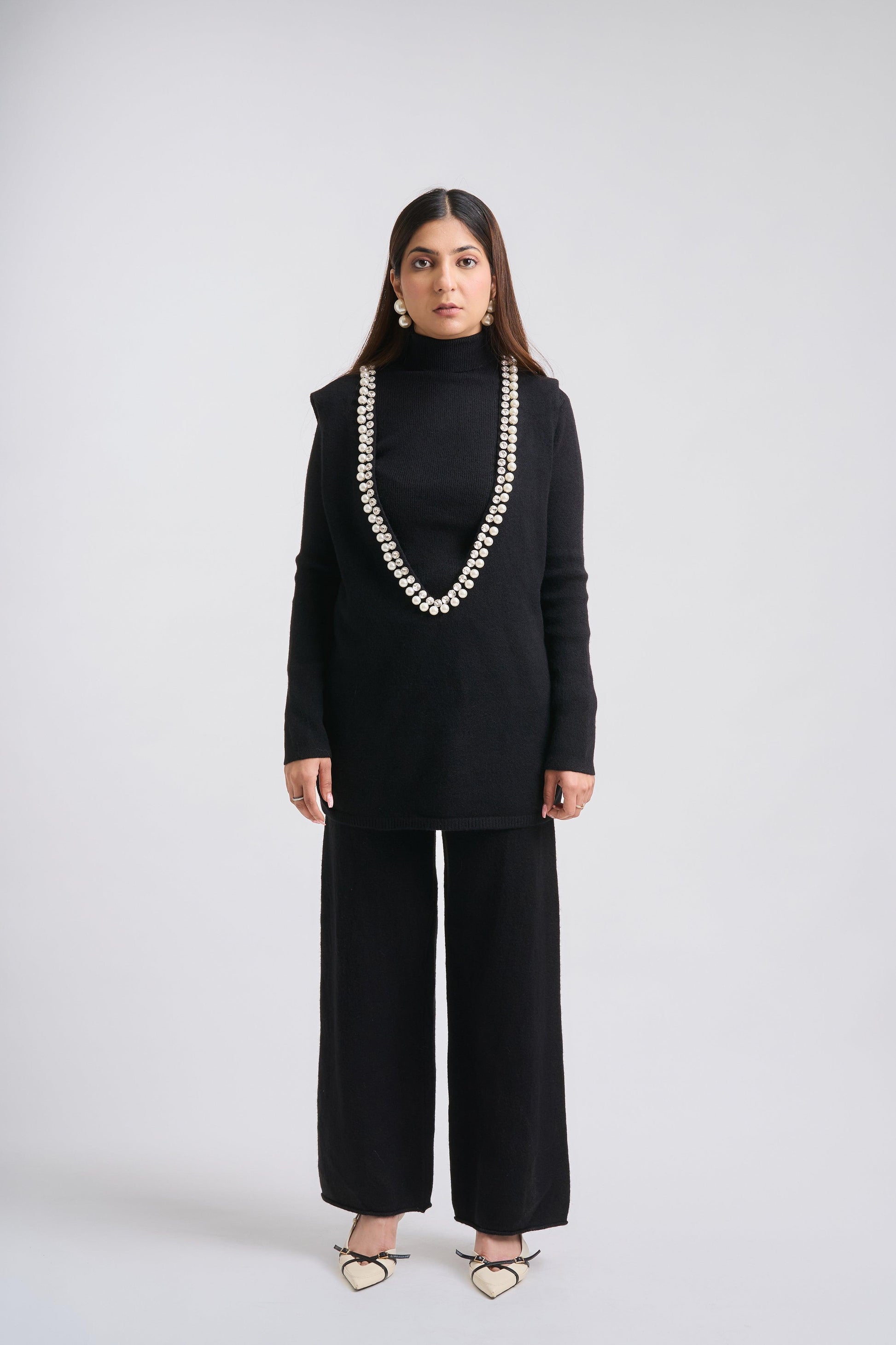Woman wearing a black outfit with a long necklace on a white background