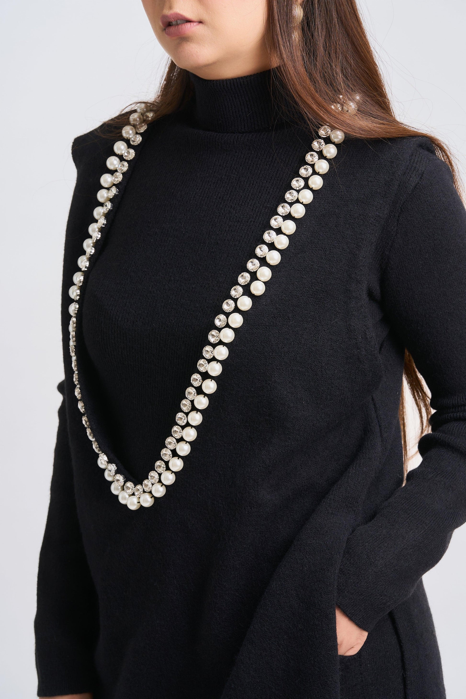 Person wearing a black outfit with a long pearl necklace on a plain background