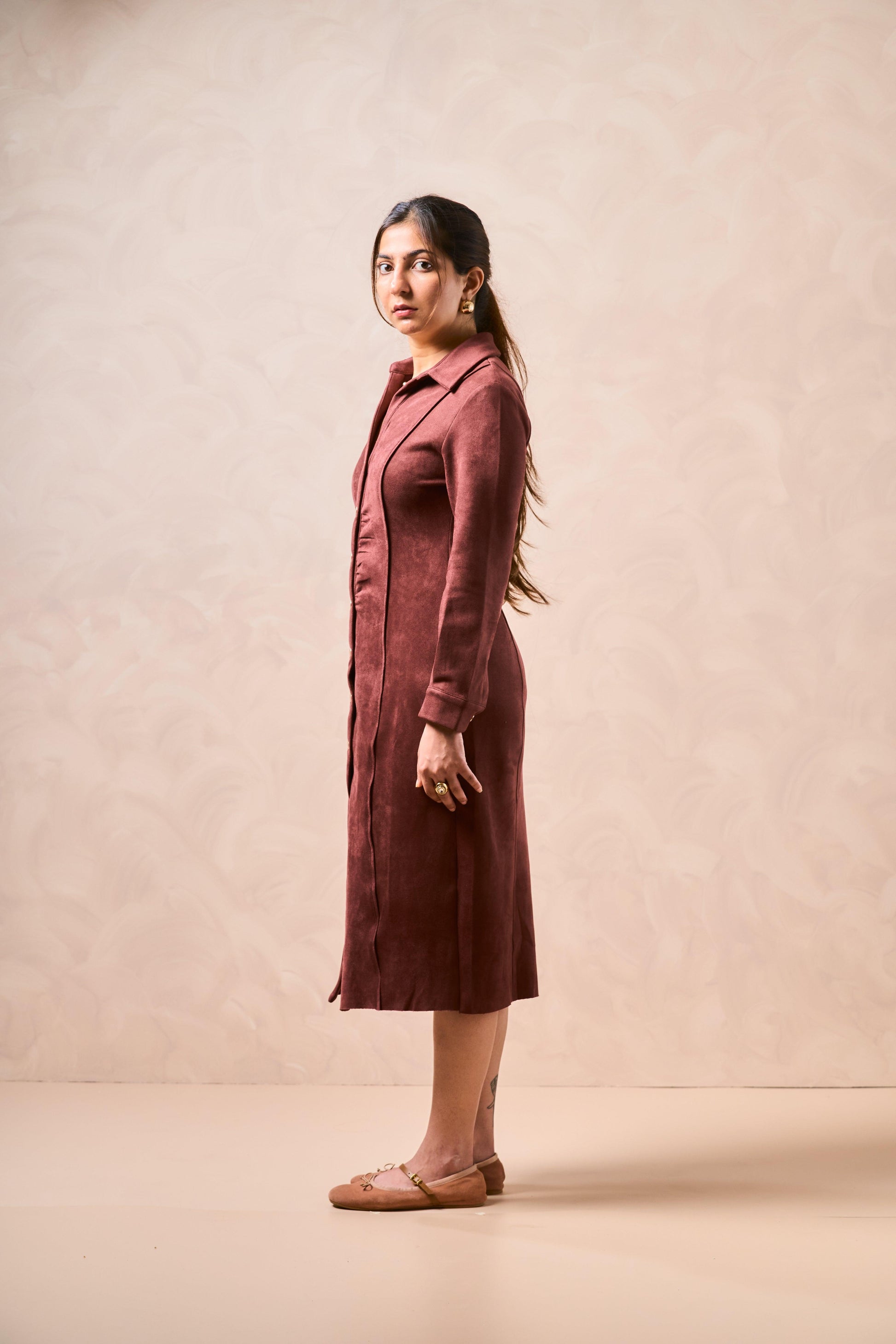 Woman wearing a long burgundy coat against a beige background