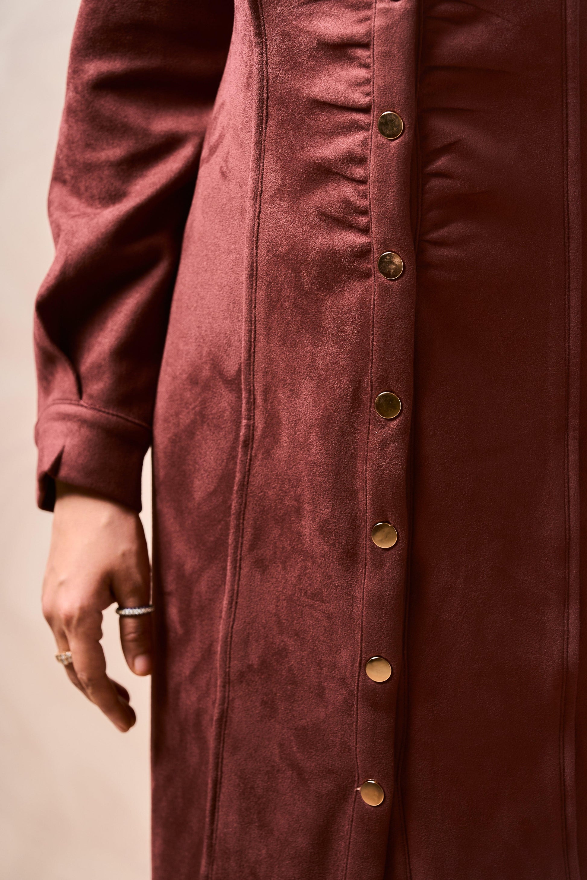 Close-up of a burgundy coat with gold buttons on a beige background