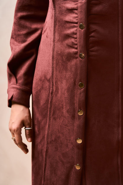 Close-up of a burgundy coat with gold buttons on a beige background