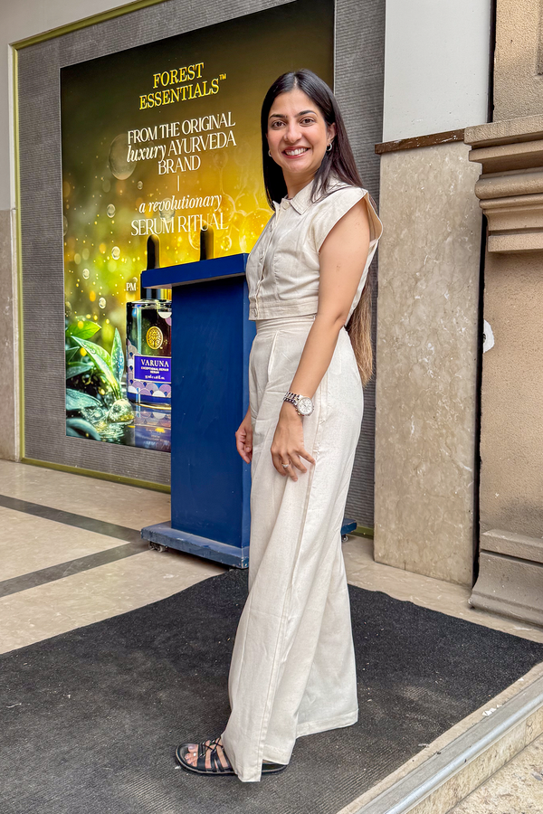 Woman in a white saree standing in front of a Forest Essentials advertisement board.