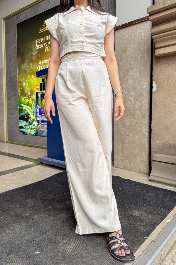 Person wearing a white outfit standing on a sidewalk with a store sign in the background.