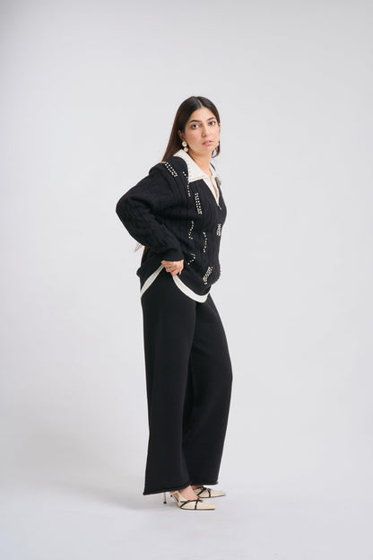 Woman wearing a black cardigan with white patterns and black pants on a white background