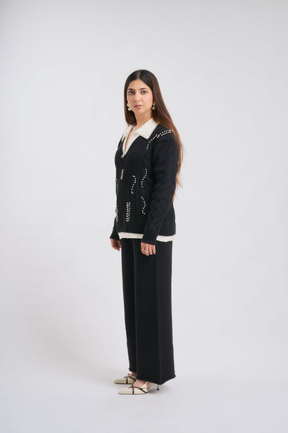 Woman wearing a black cardigan with white trim on a white background