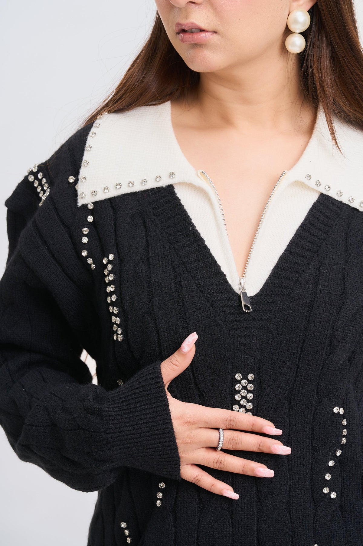 Person wearing a black cardigan with pearl embellishments on a light gray background