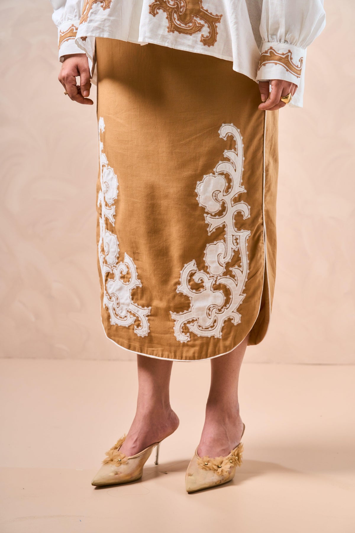 Brown skirt with white lace details worn by a person on a beige background