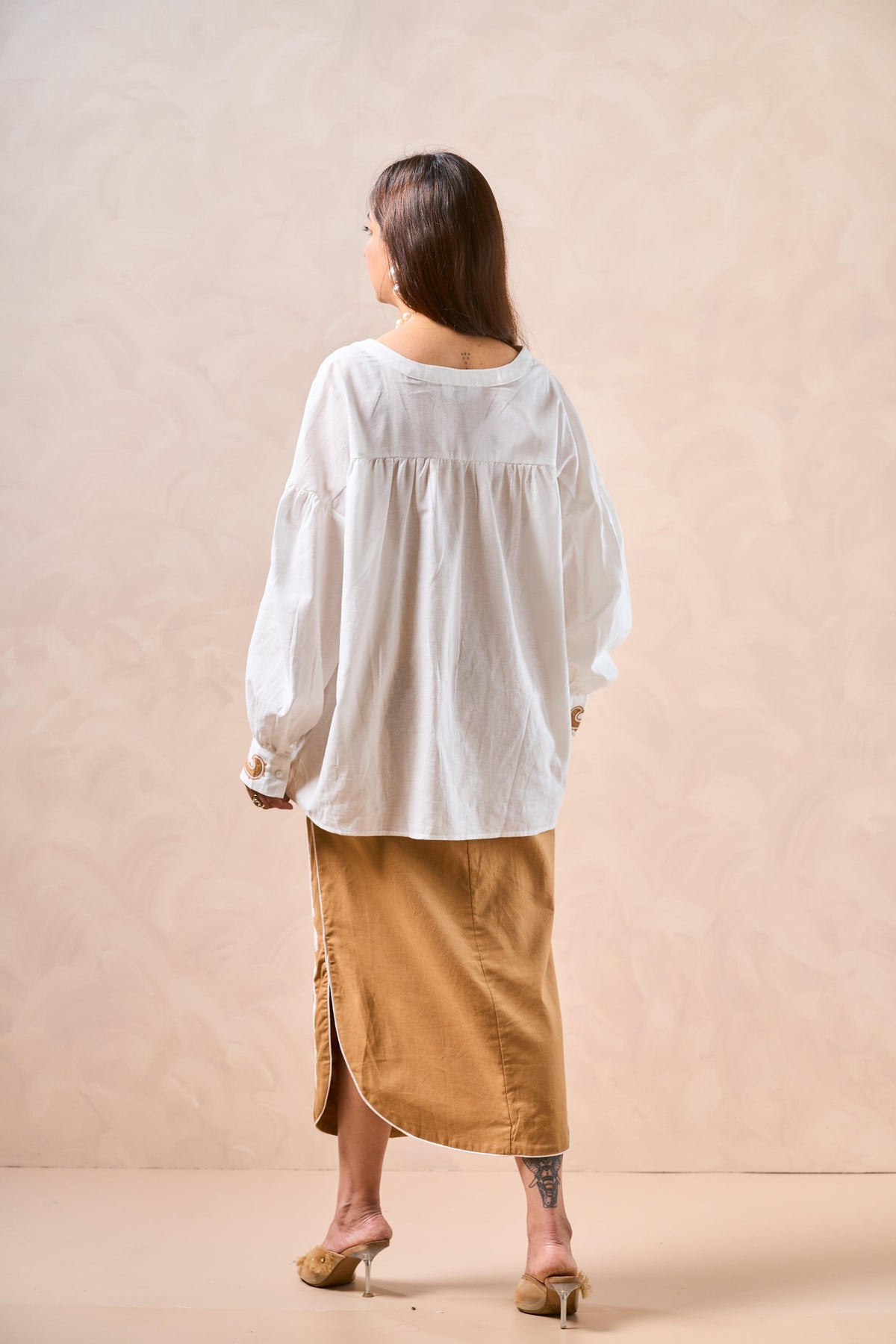 Woman wearing a white blouse and tan skirt against a beige background
