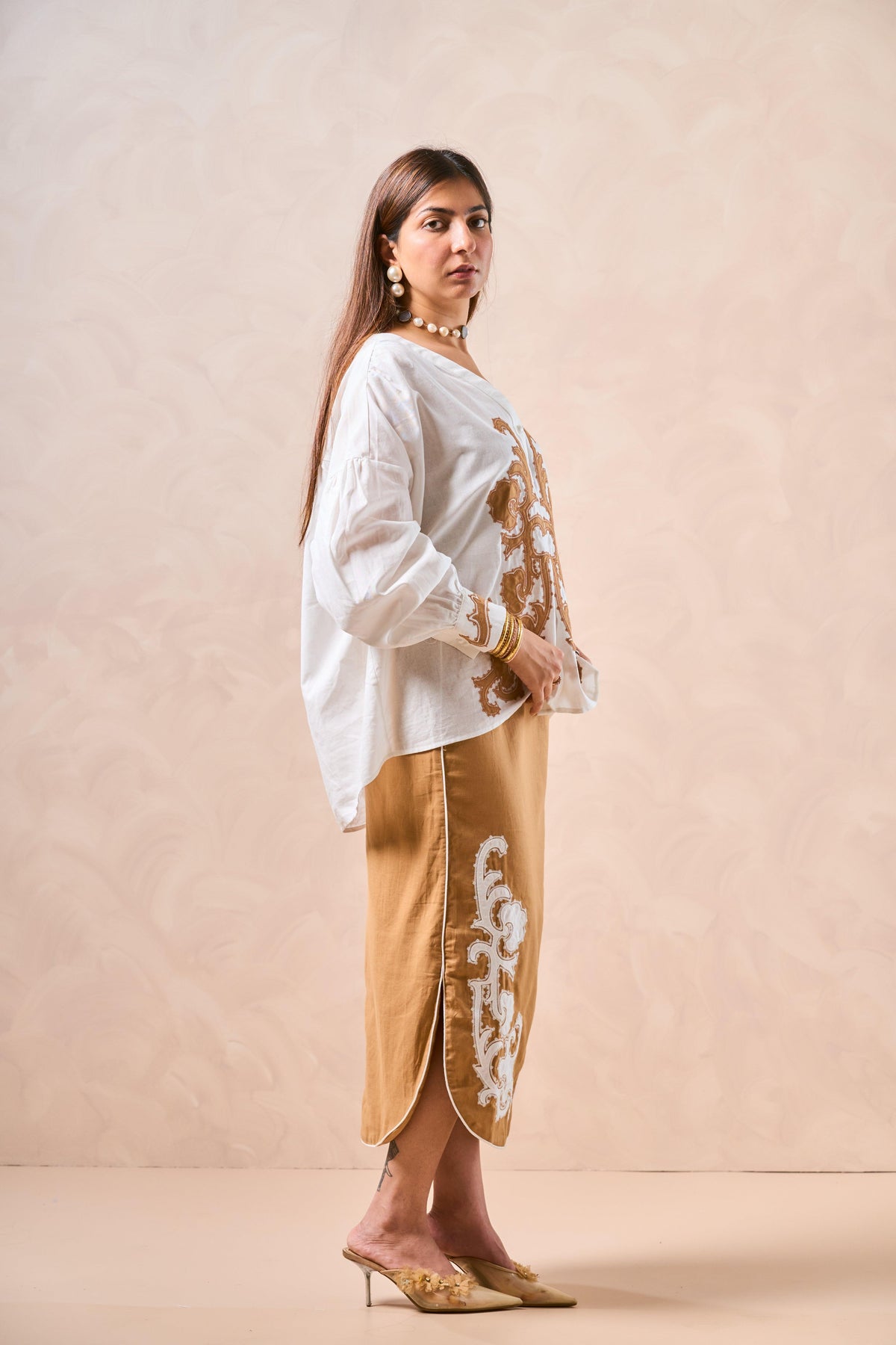 Woman wearing a white blouse with floral embroidery and a beige skirt with floral patterns on a beige background