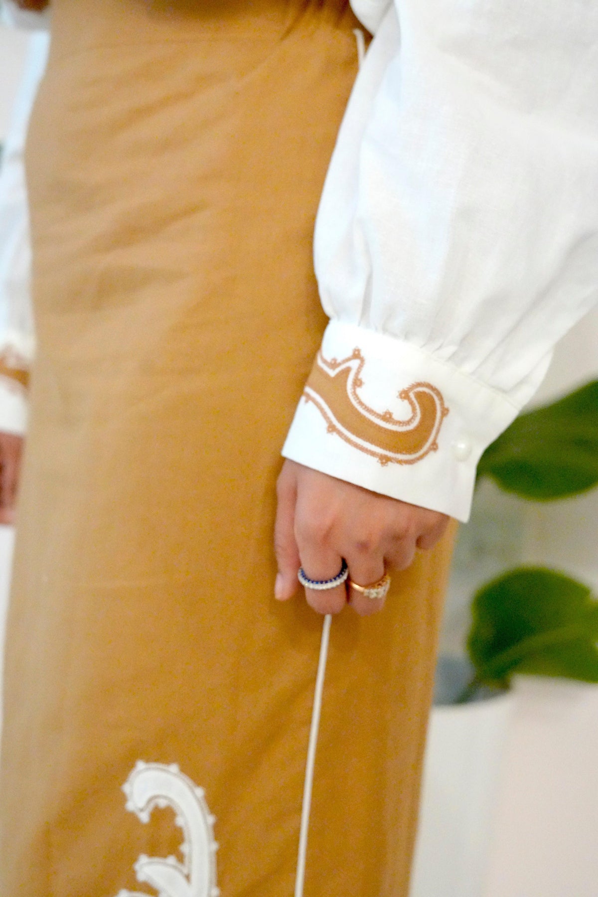 Person wearing a white blouse with decorative cuffs and a mustard yellow skirt.