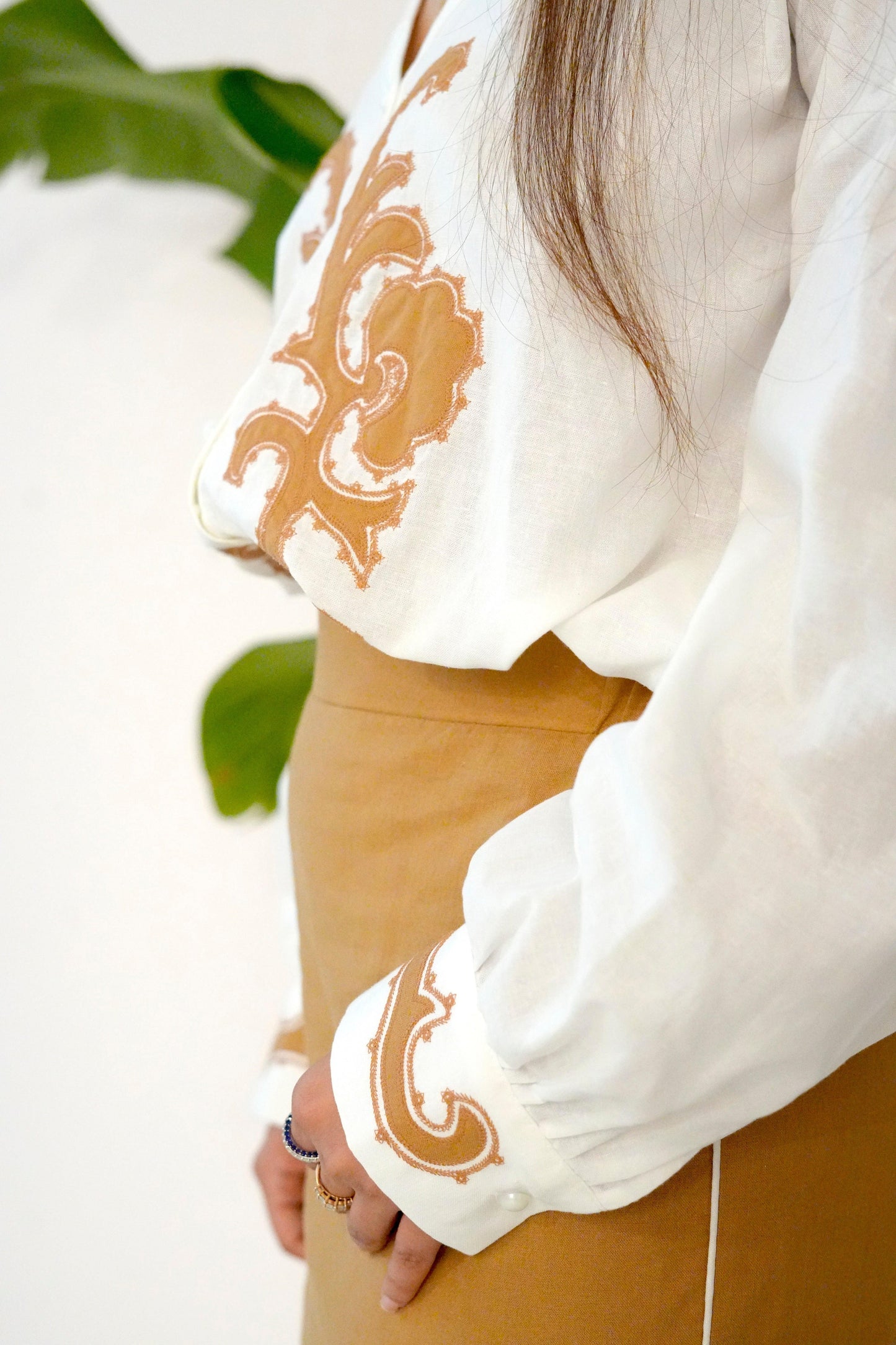 Close-up of a person wearing a white blouse with brown embroidery, holding a plant.