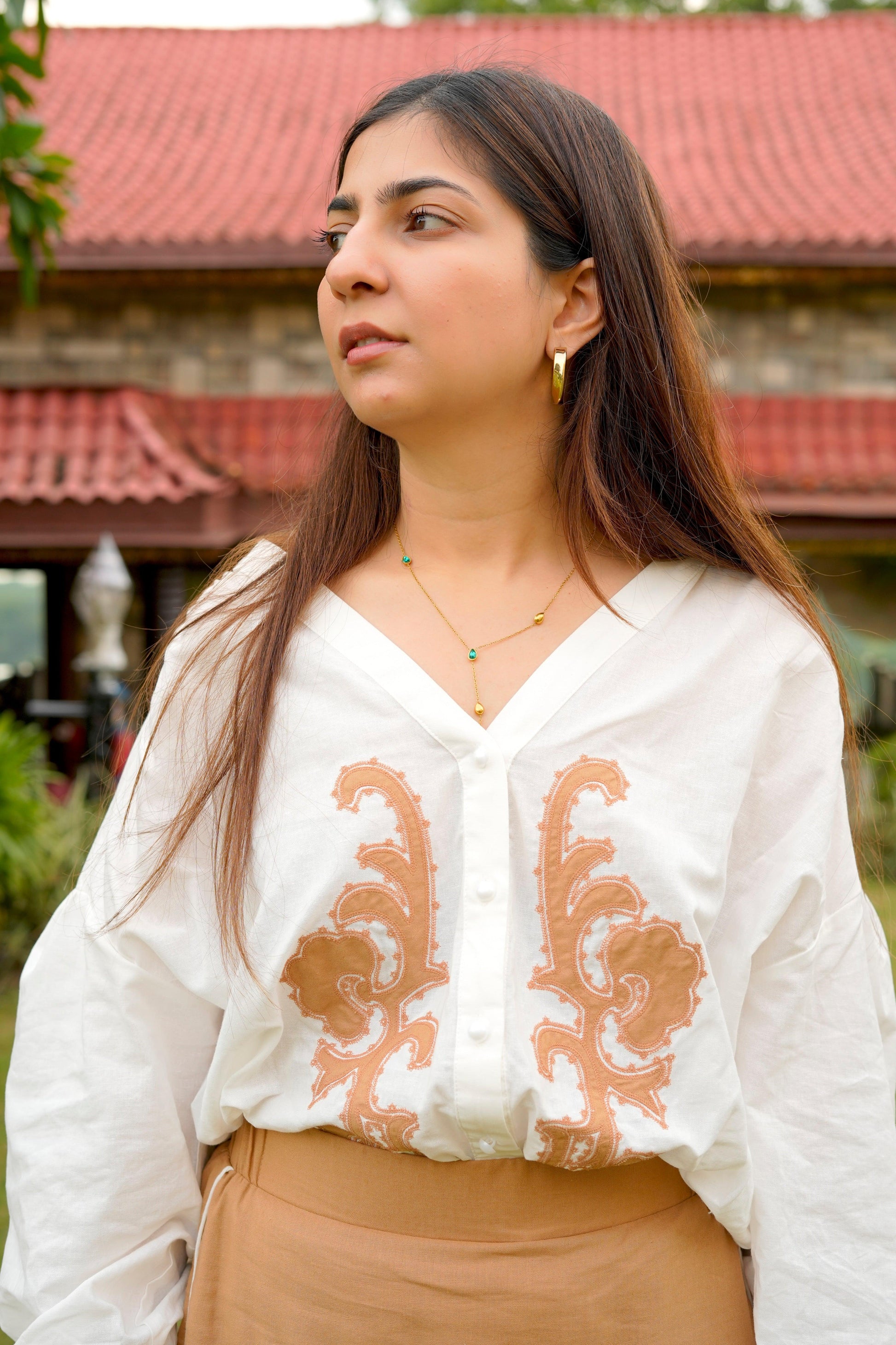 Woman wearing a white blouse with brown embroidery and beige pants outdoors.