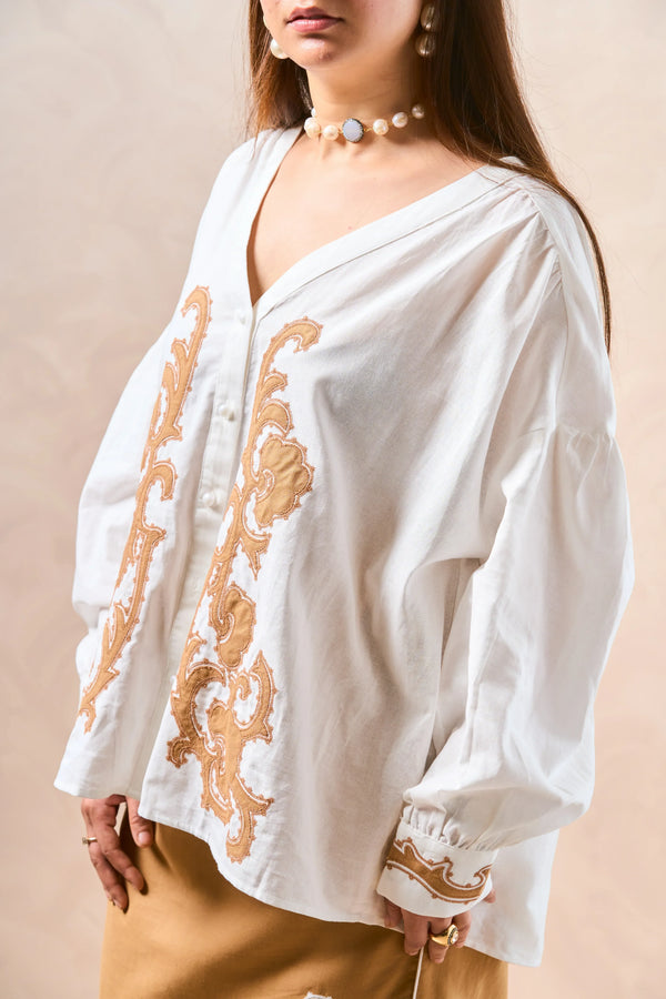 White blouse with gold embroidery on a beige background
